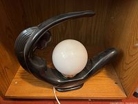 Side angle view of black sculptural figure lamp holding white globe light, showing the overall design and form.