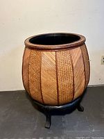 Front angle photo showing the woven rattan planter on its black stand against a neutral background.