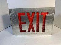 Front view of exit sign showing red 'EXIT' letters on stainless steel background wrapped in plastic.