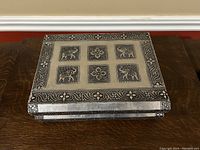 Top view of silver jewelry box showing embossed elephants and flowers in square panels and ornate floral borders.