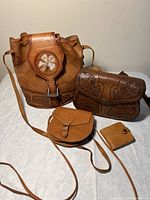 Four handmade leather purses and wallet displayed on white surface showing details of shape, straps, closures and designs.