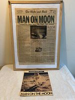 Framed Globe and Mail front page with headline about moon landing and loose Toronto Daily Star edition showing astronaut on moon.