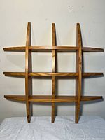 Front view of the wooden Mid-Century Modern curved wall shelf mounted on a wall, showing three horizontal shelves intersected by three curved vertical supports.