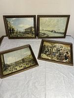 Four framed prints laid on a white cloth showing different European scenes including harbors and city squares