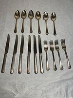 Flatware pieces arranged on fabric showing 6 spoons at top, 6 knives below, and 4 forks on right, showcasing condition and number of items.