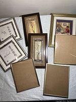 Lot of assorted picture frames including framed Asian calligraphy prints, floral prints, and a colored print of a man at piano, plus empty frames or frame backs.