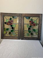 Front view showing both stained glass panels side by side with visible rose and leaf design in wooden frames.