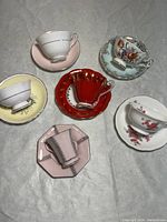 Overview of six tea cups and saucers arranged in circle on white cloth