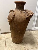 Full view of tall terra cotta vase showing cylindrical shape and decorations