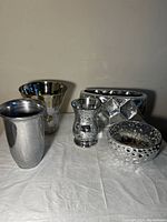Five decorative items displayed on a cloth surface; includes metal vases, a pot, and glass bowls