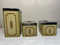Three vintage EKCO kitchen tins in beige with chrome lids placed side by side showing the front with embossed initials S, C, and F.