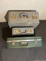 Top-down photo of the two McBrine hard cases stacked: a green case on bottom and two gray ones stacked above, showing their exteriors and handles.