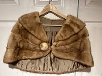 Front view of vintage mink stole hanging on a wooden hanger showing plush light brown fur and satin lining edges.
