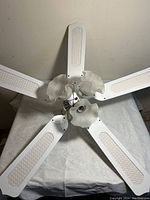 Top view of the white ceiling fan showing five blades with textured panels and three frosted glass light shades in the center.