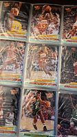 Basketball cards in plastic sleeves within a binder showing various players, identifiable by their NBA Hoops 1991-92 design and presence of multiple player images in game action.