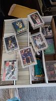 Large box filled with many stacks of sports cards including basketball and hockey cards, some in protective sleeves.