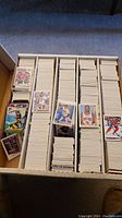 Box containing a large number of mixed sports trading cards, mostly basketball, football, hockey, and baseball, shown neatly stacked in rows.