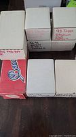 Photo of seven cardboard boxes containing various sports trading card sets with handwritten labels visible on the top and side of boxes.