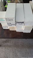 Photo of multiple white storage boxes stacked with handwritten labels such as '93 Score Football', '91-92 U.D. Hockey 1-500'