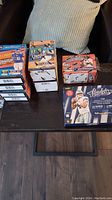 Multiple opened boxes of football trading card packs placed on a table with a pillow on a chair behind them.