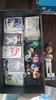 Photo showing stacks of sports trading cards, several baseball bobbleheads, and poker chips inside a box with a Mookie Betts bobblehead nearby.