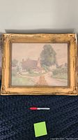 Full view of framed watercolor landscape painting by Ethel Hughes showing cottages, trees, and a pathway.