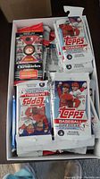 Box of assorted unopened and opened baseball card packs including Topps 2022 Series 1 and Panini Chronicles
