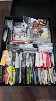 Top view of a black box filled with various opened and unopened sports card packs stacked tightly, showing some player images and text on the packs.