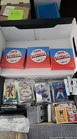 Top view of three Topps Baseball Living Set boxes and assorted sports cards laid out in box including player's cards in sleeves.