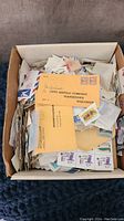 Box filled with assorted vintage US postage stamps and envelopes including some air mail envelopes and various sizes.