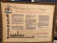 Framed Canadian Bill of Rights document displayed with visible broken glass across upper right side but document print unaffected.