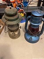 Pair of vintage lanterns: one Coleman metal lantern with green top and another blue lantern with red glass globe.