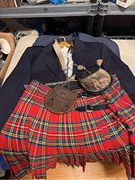 Full overview of navy jacket, white shirt, red tartan kilt, two sporrans, belts and chain