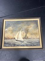 Framed oil painting showing a sailboat on water with an industrial cityscape in the background, image under good lighting showing texture and detail.