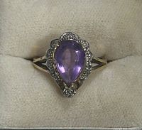 Front view of the ring showing the pear-shaped amethyst surrounded by small clear accent stones set in 10k yellow gold.