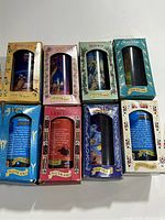 Photo showing the front side of the boxed Disney collector glasses with movie titles and images visible. Glasses arranged showing the Pinocchio, Beauty and the Beast, Jungle Book, Snow White, Peter Pan, The Lion King, Aladdin, and The Fox and the Hound boxes.