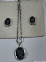 Front view of necklace and earrings displayed on white cloth background showing detailed cameo carvings and chain.