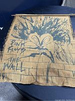 Front view of Pink Floyd The Wall burlap flag showing stylized screaming face graphic and text.
