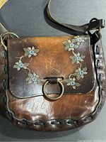Front view of vintage brown leather shoulder purse with blue floral detail and a ring closure on the flap.