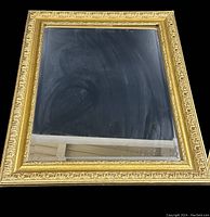 Front view of vintage rectangular wall mirror with ornate gold-tone frame showing detailed floral and scroll design.