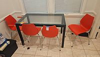 Five red hard plastic chairs placed around a rectangular glass-top table with black metal frame, showing the full lot