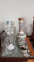 Photo of four crystal decanters and one ceramic decanter on a tray with metal chain bottle tags for various spirits.