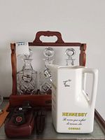 Overview of wooden decanter case with three crystal decanters, ceramic pitcher, leather tool pouch and utensils