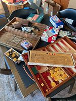 Overview of several board games on a table, including backgammon boards with pieces, cribbage board, boxes of playing cards, and dice cases.