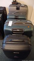 Front view of three hard shell roller suitcases (black, dark green, silver) and soft side bag