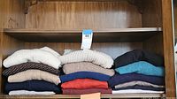 Stack of folded men's sweaters in various colors including beige, brown, navy blue, red, turquoise, and black.