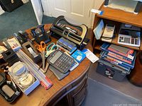 Overview of office supplies on round wooden table including hole punchers, scissors, calculators, tape dispensers, staplers.