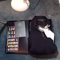 Folded dark navy wool cardigan sweater with tags visible on top next to a black case and a booklet.