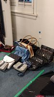 Five handbags and small accessories arranged on floor in front of wall