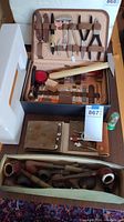 Overall view of opened tan tool case, suede pouch and tub of wooden pipes